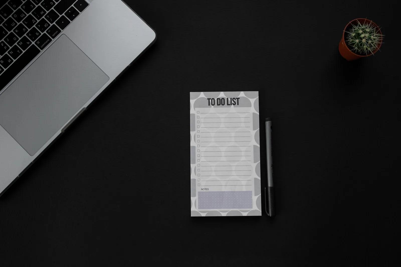 To-do list beside a laptop on a dark workspace