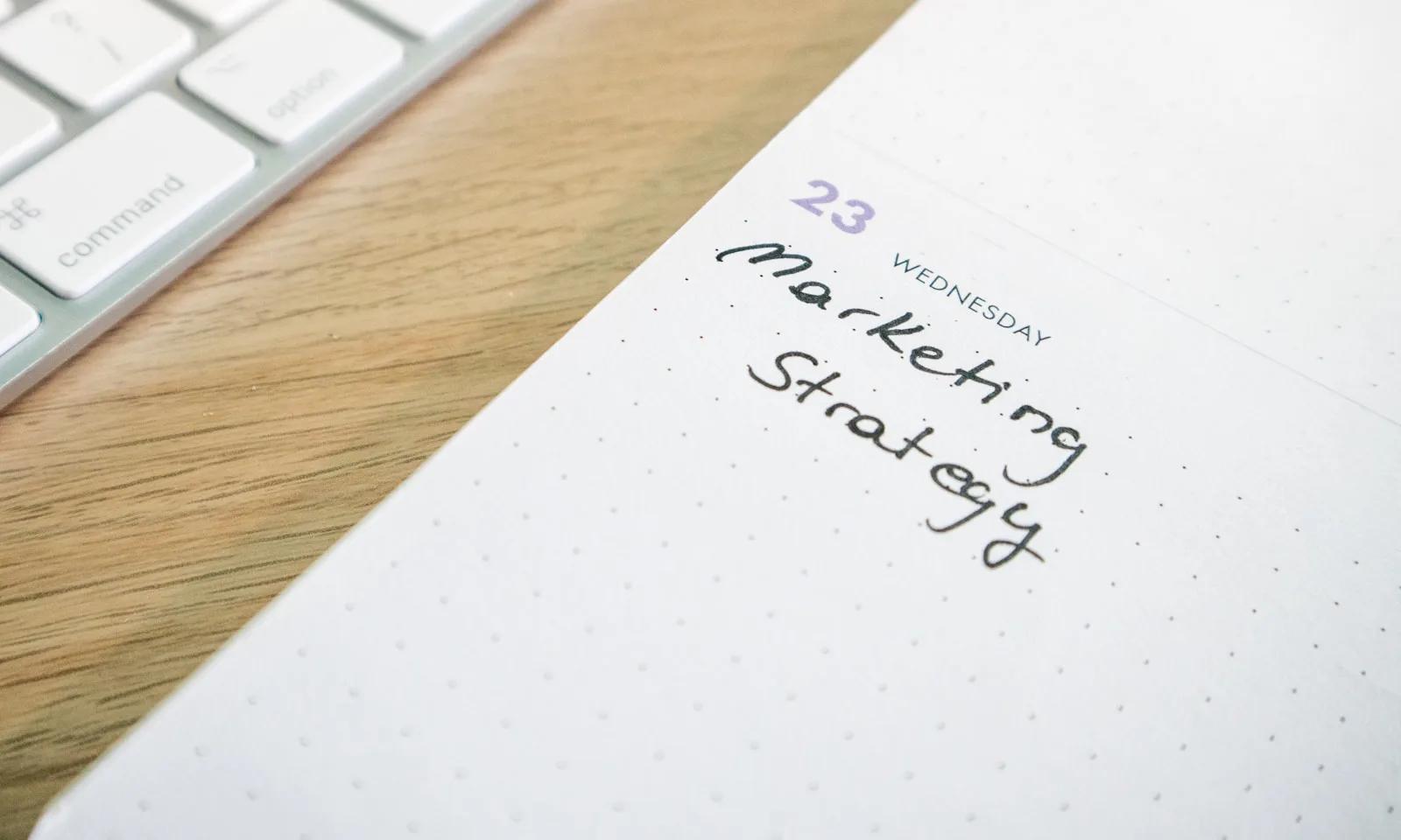 Notebook page labeled marketing strategy beside a keyboard on a desk